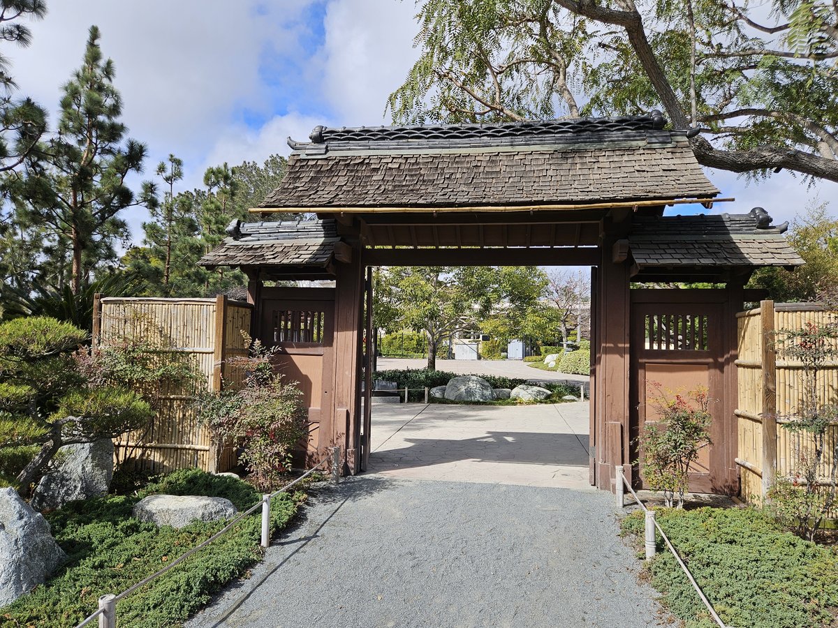 The traditional wooden entrance gate of the Japanese Friendship Garden in Balboa Park, with a tiled roof and a stone path leading through
