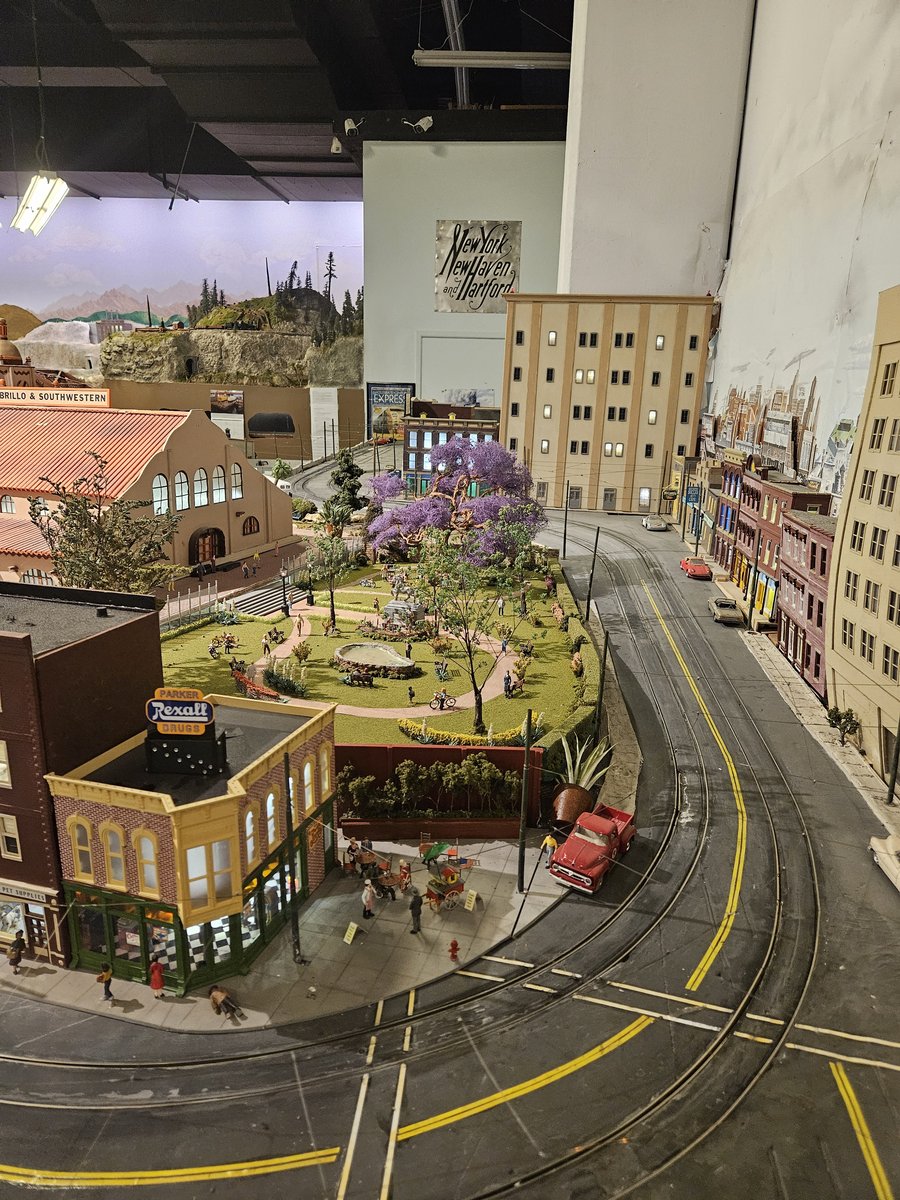 Close-up of a street scene in the model railroad display at Balboa Park, with miniature buildings, a yellow tram and a jacaranda tree in bloom