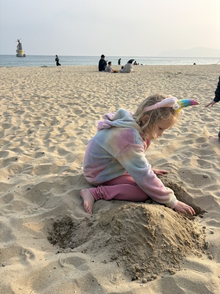 Girl in unicorn headband digging in the sand at Haeundae Beach, Busan