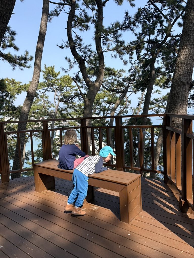 Two kids sitting on a bench at a sea viewpoint in the park near Songjeong Beach