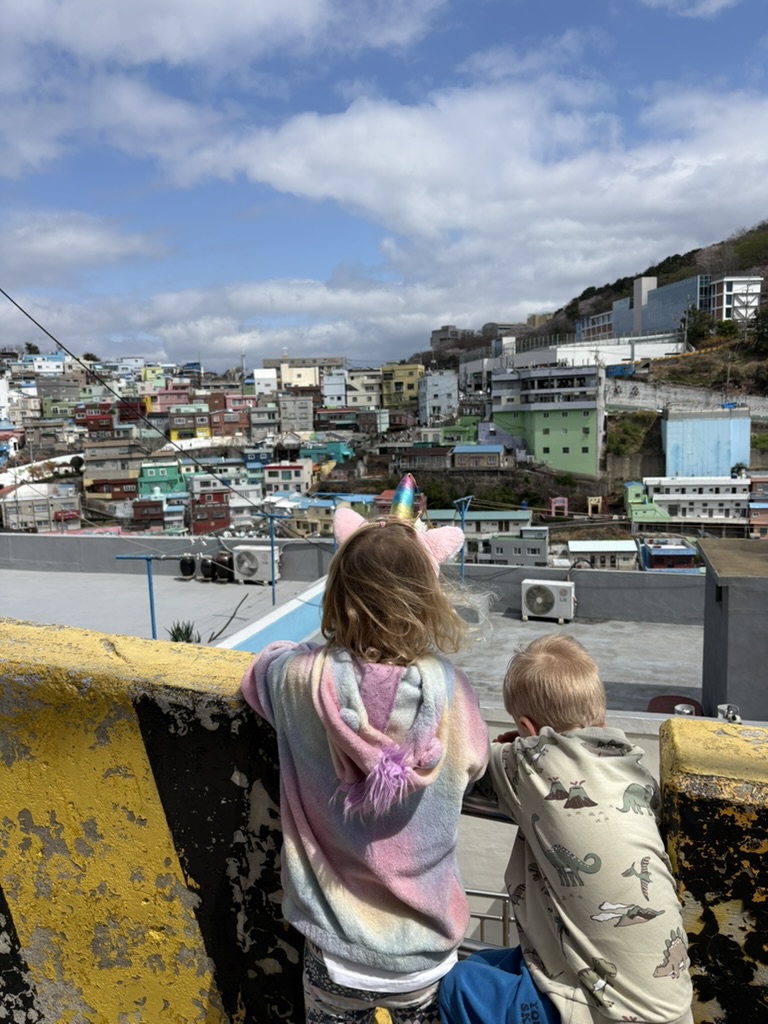 Two kids leaning on a yellow railing at a Gamcheon rooftop viewpoint