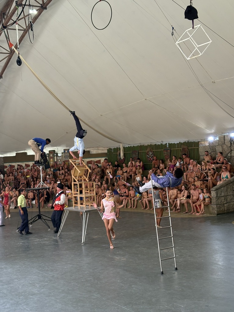 Acrobats performing a balancing act on stacked chairs in the covered theatre at Caribe Bay, watched by a large crowd