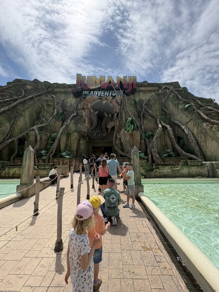 Kids walking toward the Jumanji: The Adventure entrance at Gardaland — stone face facade, rope barriers, turquoise pool