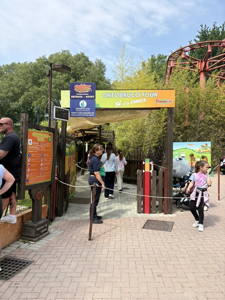 Ortobruco Tour entrance at Gardaland — colourful sign, entry gate, a child walking in with a stroller nearby