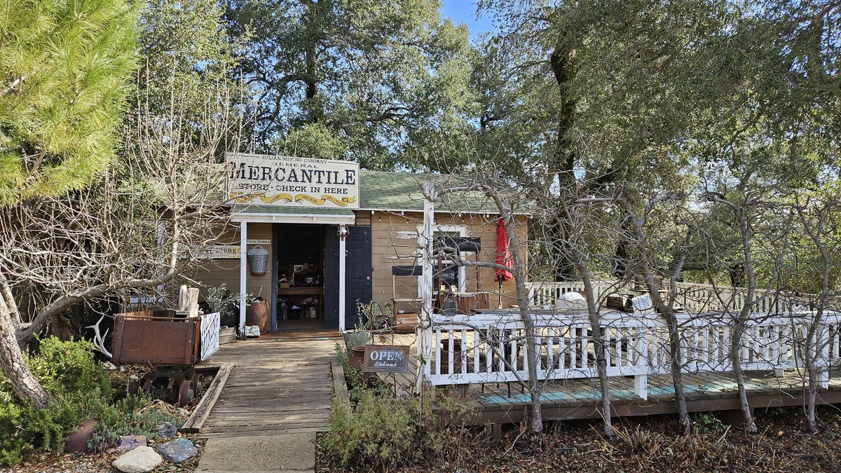 The historic Mercantile building on Julian's main street, a rustic wooden storefront surrounded by pine trees, capturing the gold rush town's atmosphere