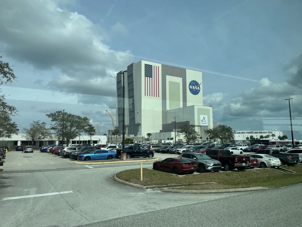 The Vehicle Assembly Building at Kennedy Space Center seen from the tour bus window, a huge hangar with a large American flag and the NASA and Artemis logos on its side