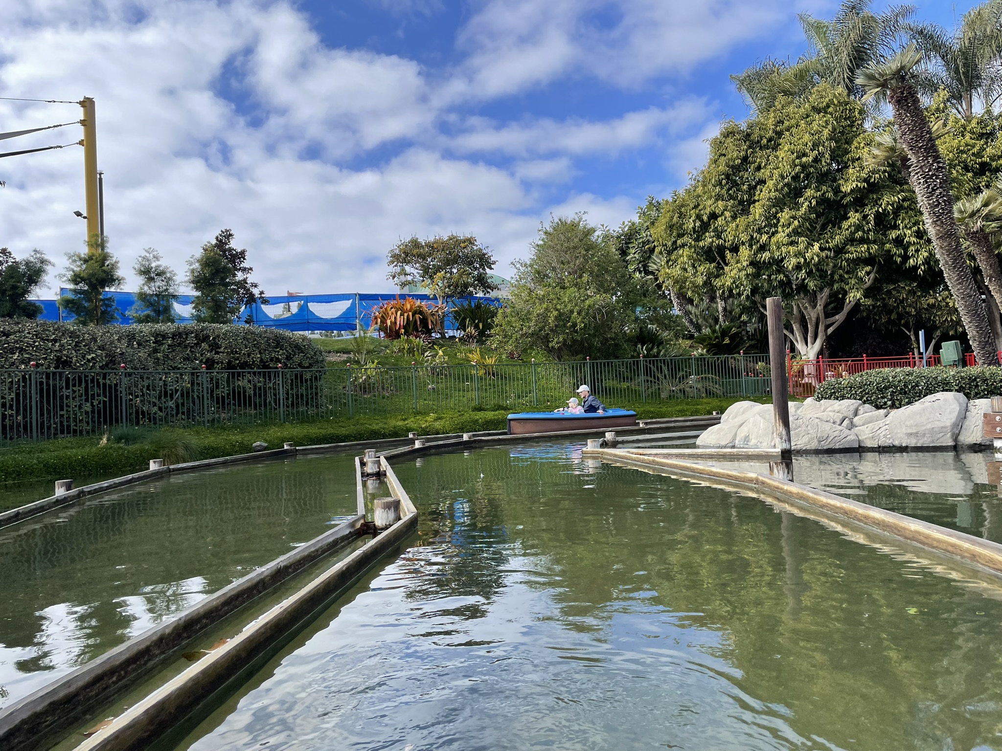A boat gliding along a canal at Legoland California with trees and the park in the background