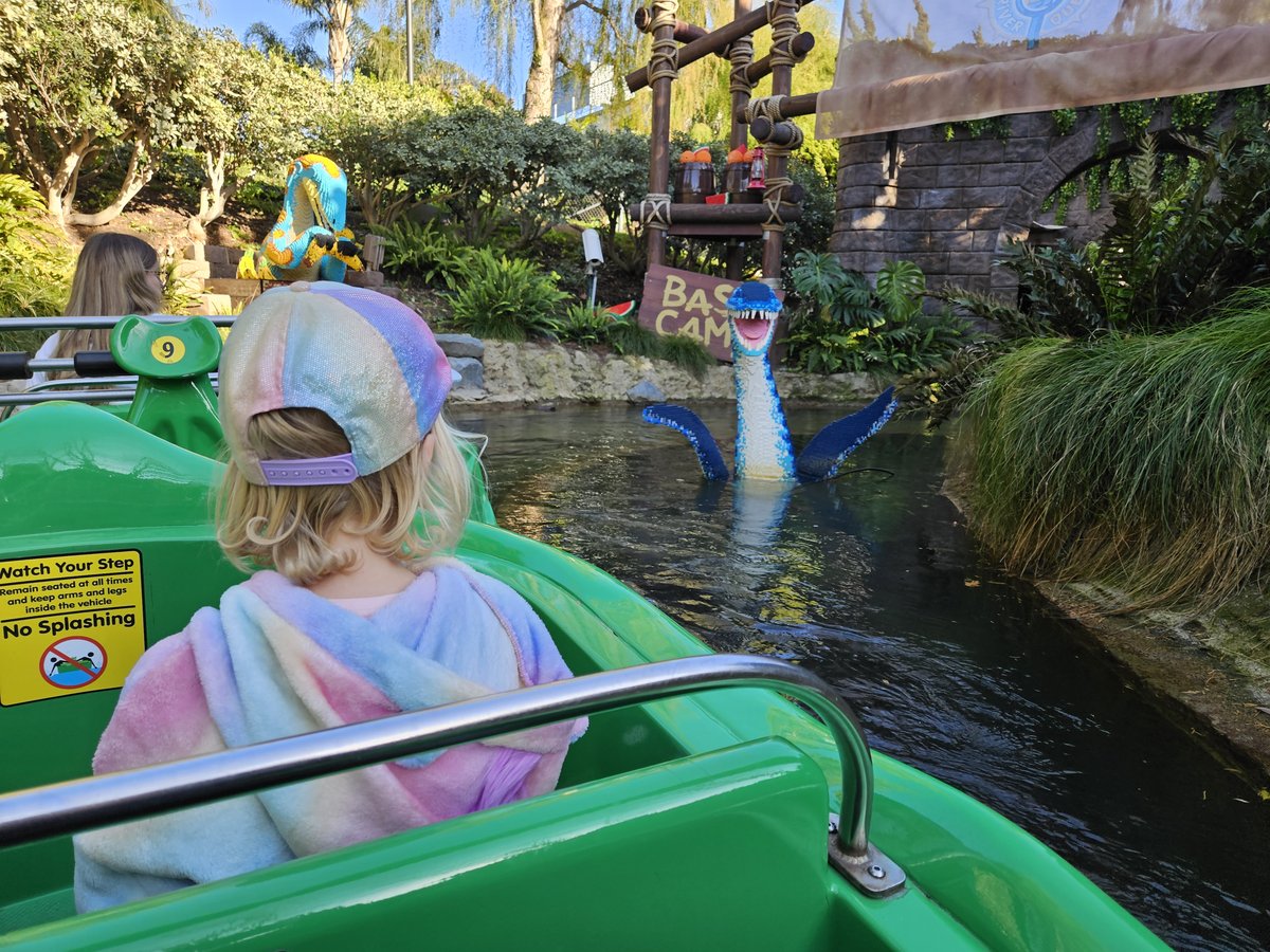 Young girl on the Dino Island boat ride at Legoland California, with a LEGO dinosaur figure emerging from the water beside the boat