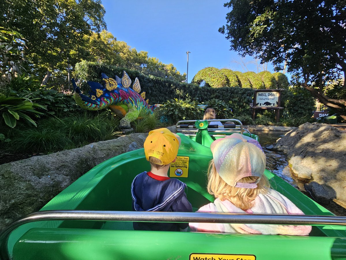 Two kids on the Dino Island boat ride at Legoland California, surrounded by LEGO dinosaur scenery along the water channel