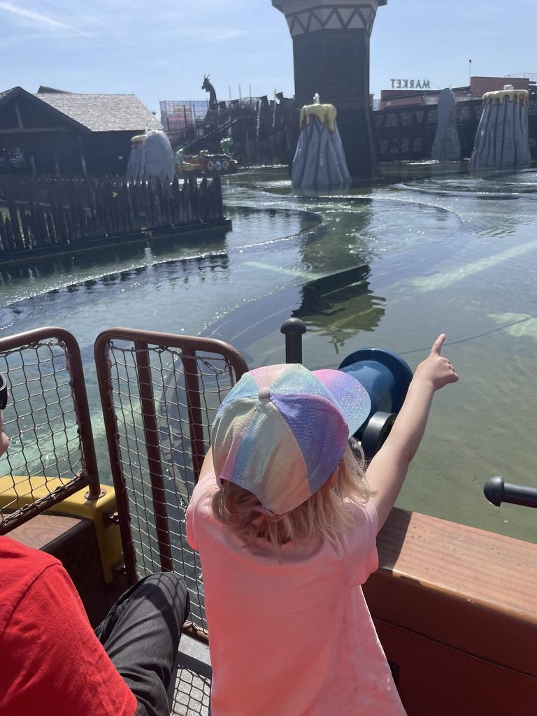 View from a themed boat ride at Energylandia looking out over water toward a viking longship and market scenery