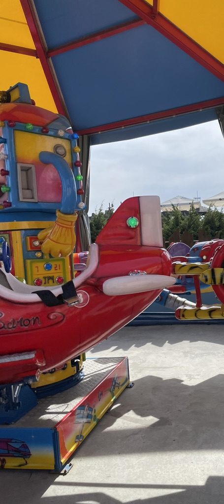 A bright red kids' aeroplane ride vehicle under a colourful striped canopy in Energylandia's Bajkolandia zone
