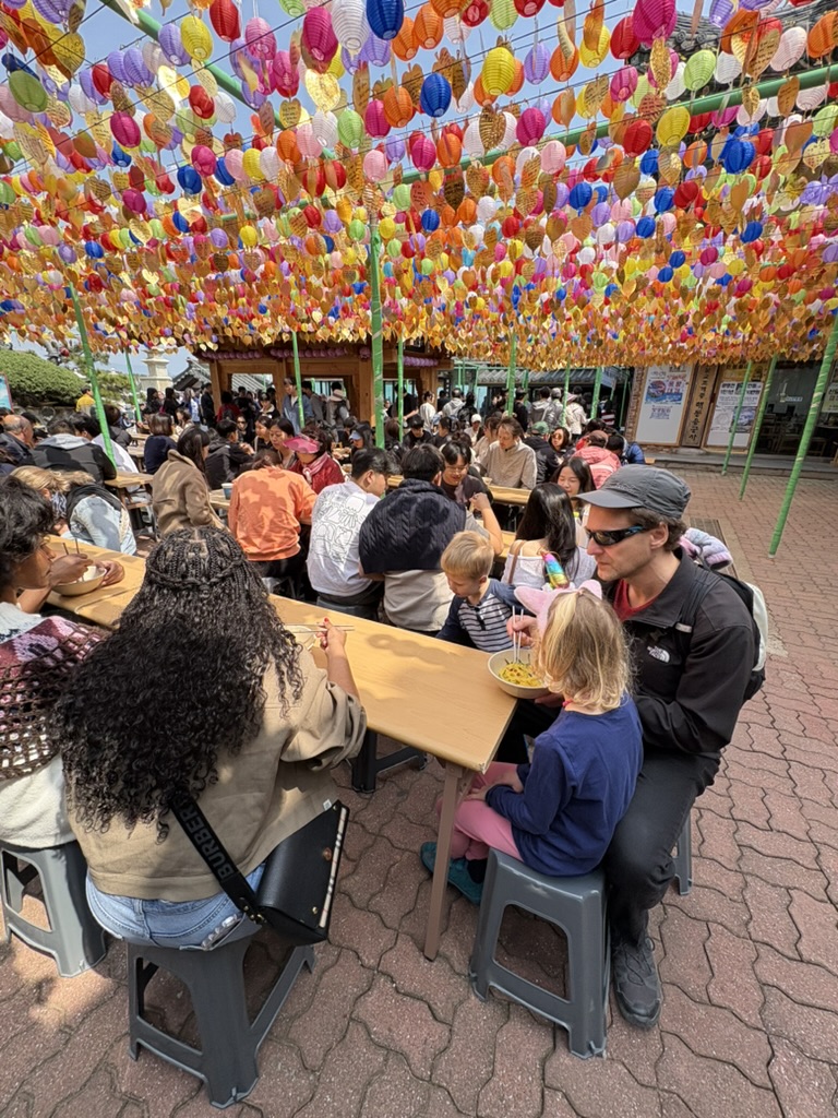 Family eating free temple noodle lunch under colourful lanterns at Haedong Yonggungsa