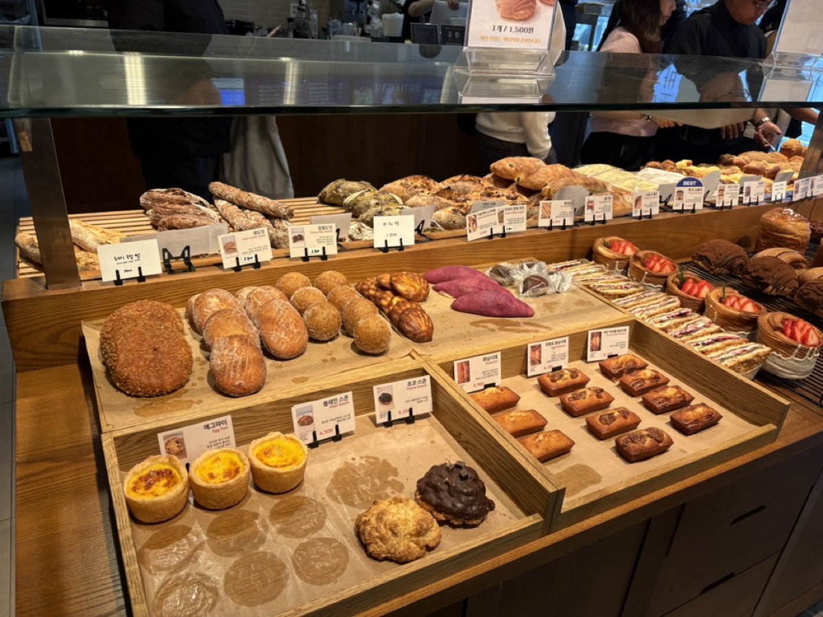 A Korean bakery display case full of breads, egg tarts, pastries and two purple sweet potatoes