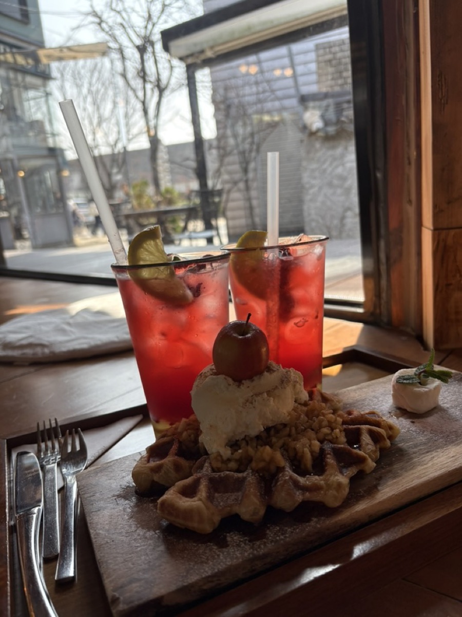 A waffle topped with cream and apple beside two iced berry drinks at a Korean cafe window