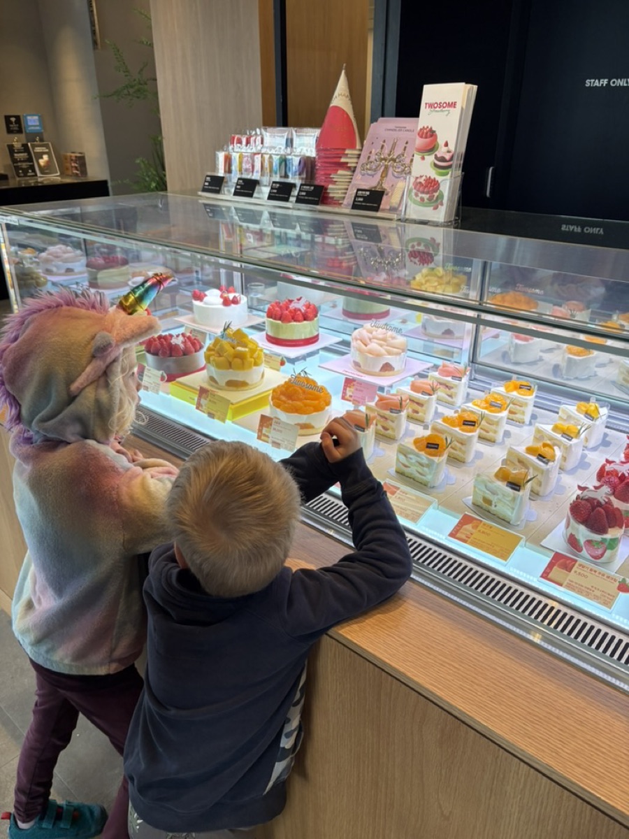 Two young kids looking into a Korean cafe cake display case full of fruit-topped cakes
