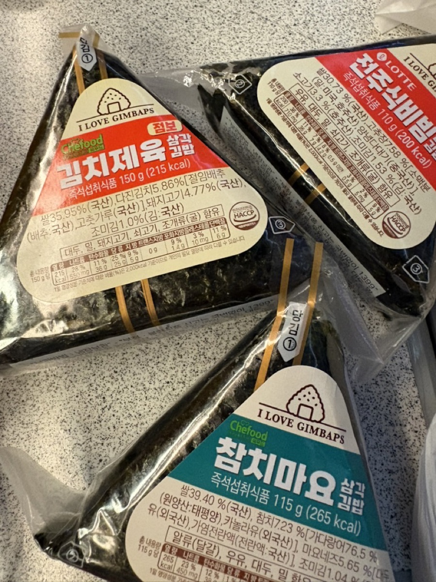 Three triangle gimbap rice balls from a Korean convenience store, including a tuna-mayo and a spicy kimchi variety