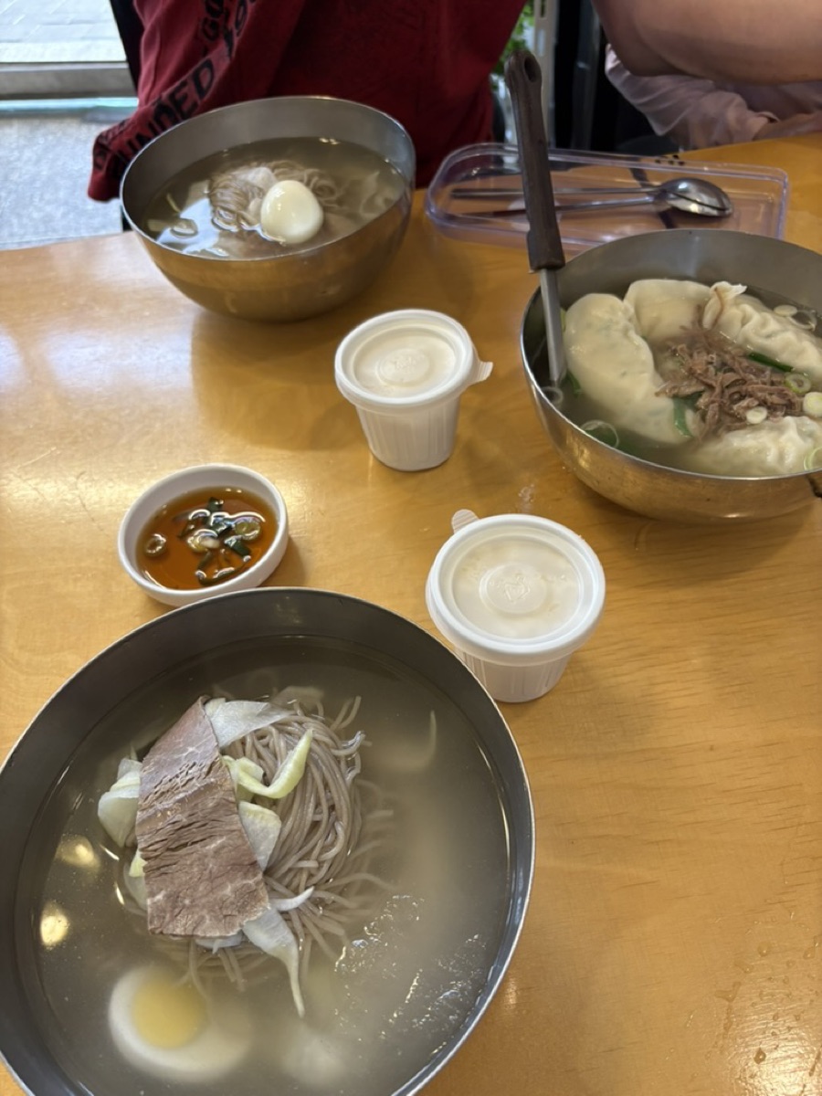 A bowl of mandu dumpling soup beside a bowl of cold naengmyeon noodles at a Korean restaurant