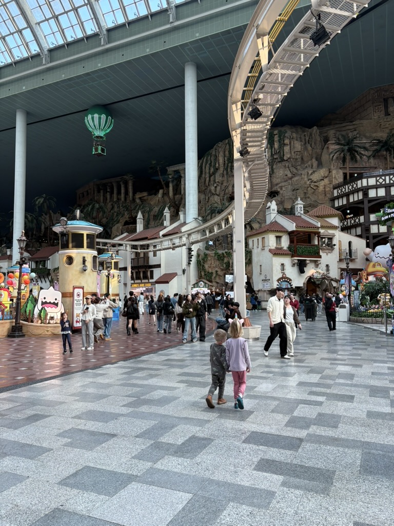 Kids walking through Lotte World Adventure dome with floating balloon and roller coaster track overhead