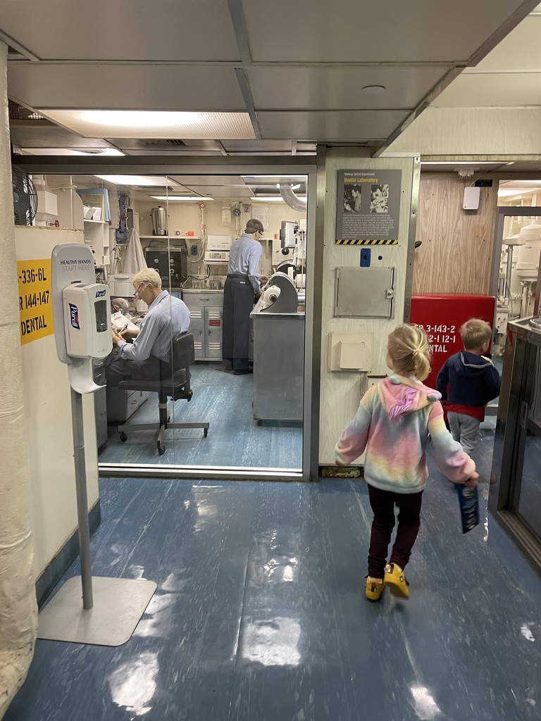 Two young children walking through the below-deck corridors of USS Midway past the dental laboratory exhibit